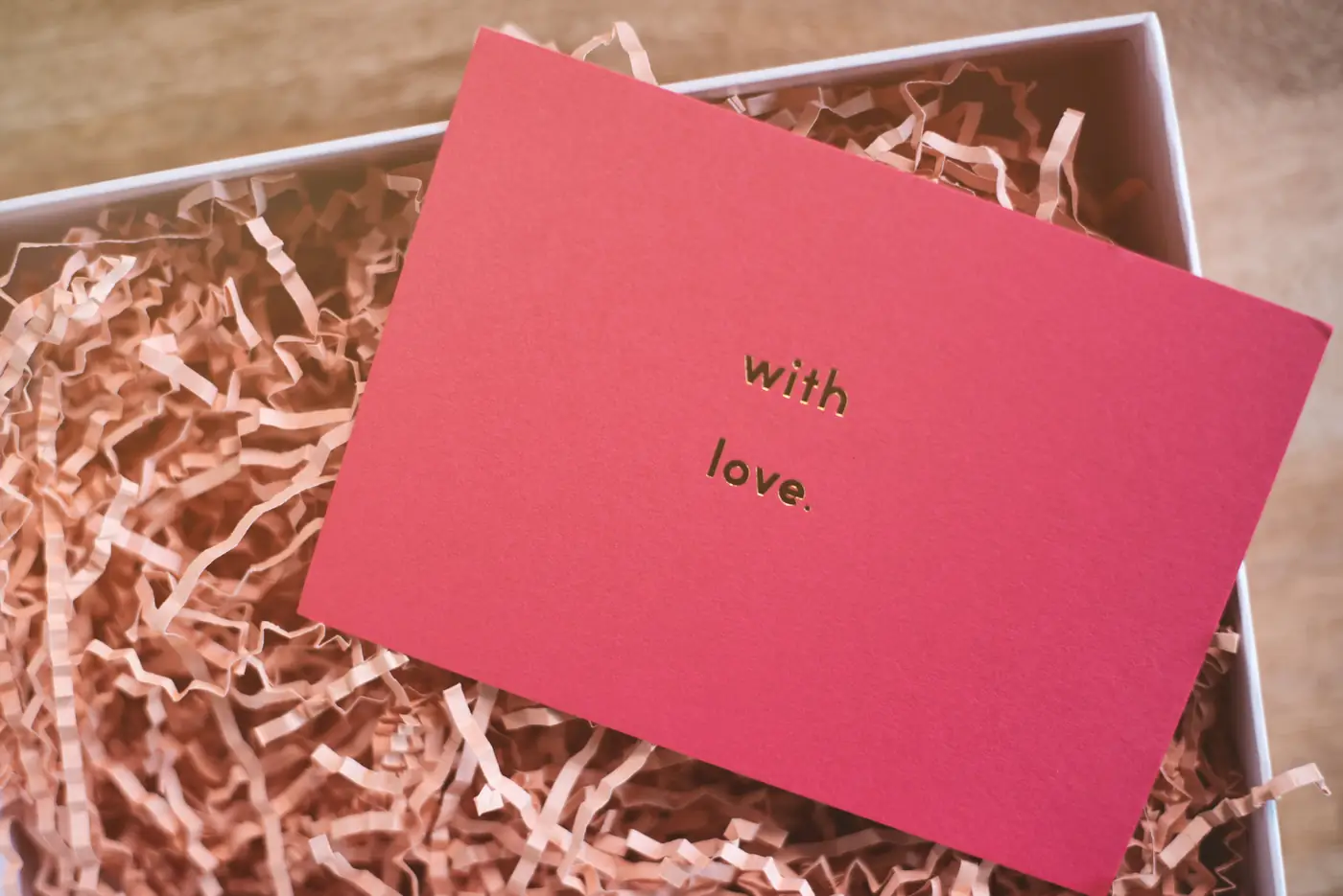 Carte rose « with love » posée sur la frisure d’une box cadeau
