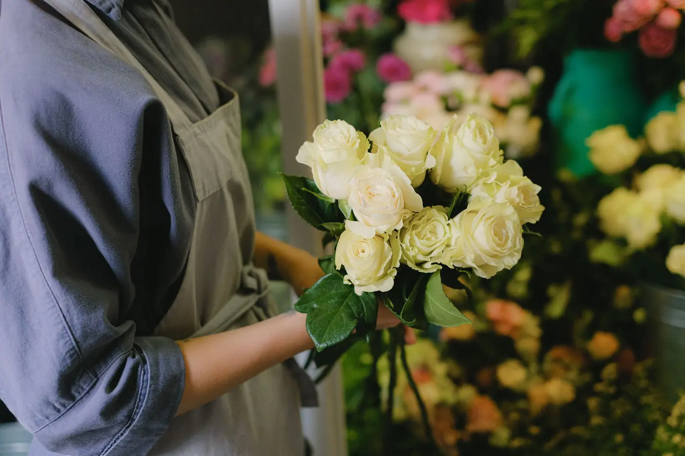 Fleuriste en tablier tenant un bouquet de roses blanches dans sa boutique